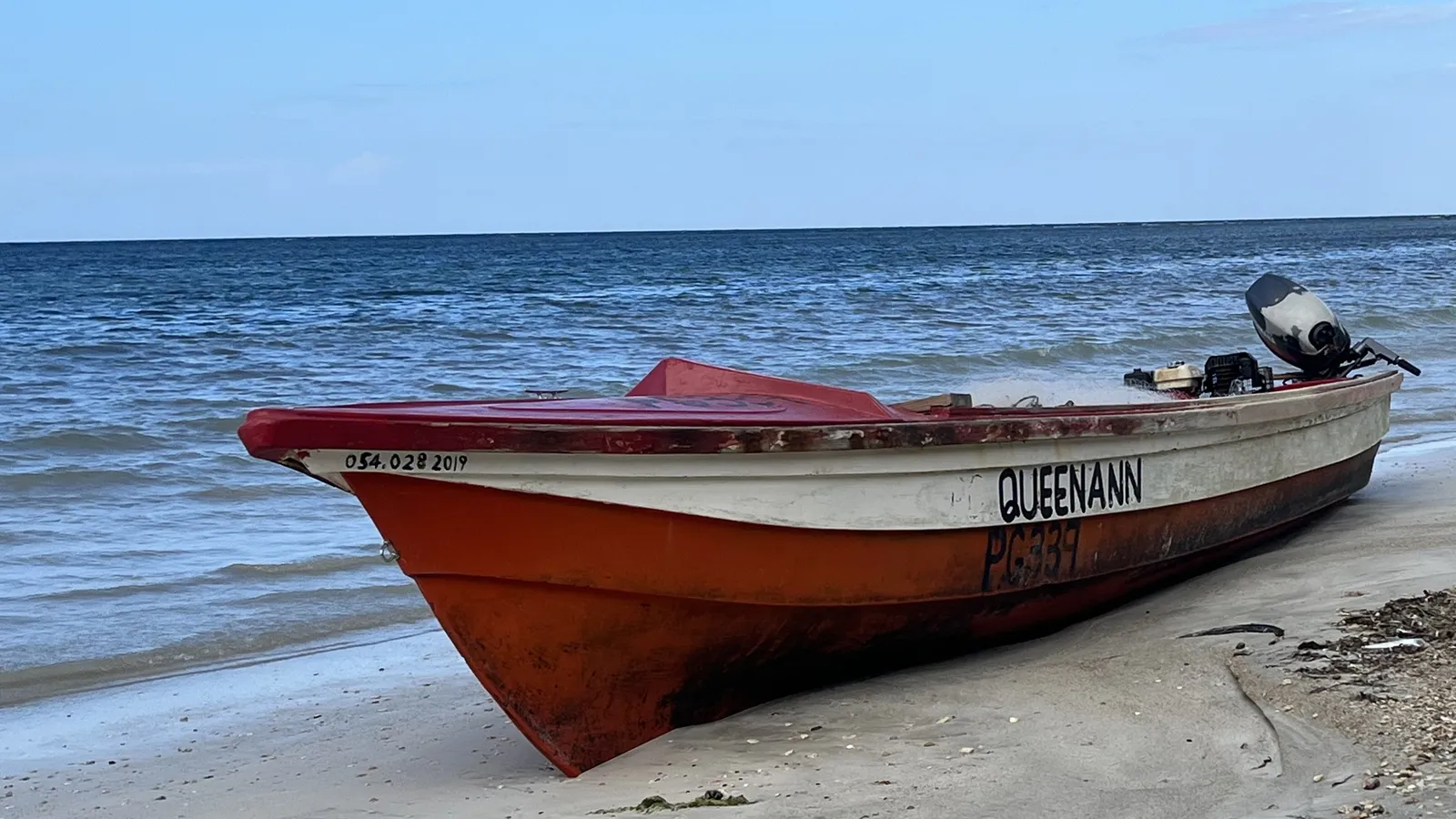 A small orange and white fishing boat drawn up on the brown-grey sand at Priory Beach, with calm open sea and a low horizon behind it